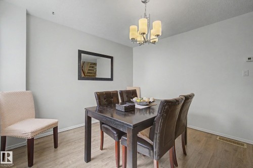 Dedicated dining area featuring wood-finish flooring, light grey wall tones, and a contemporary chandelier with frosted glass shades - 17305 60 Ave, Edmonton, AB 