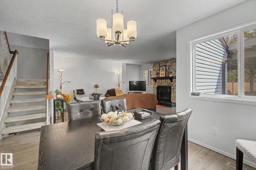 Open-concept living space featuring wood-finish flooring, a stone fireplace, and a contemporary chandelier - 17305 60 Ave, Edmonton, AB 