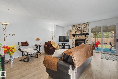 Living area featuring wood-finish flooring, a stone fireplace with a dark mantel, and sliding glass doors opening to the exterior - 17305 60 Ave, Edmonton, AB 
