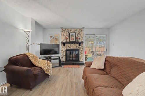 Living area featuring a stone-clad fireplace with a dark mantel, wood-finish flooring, and white walls - 17305 60 Ave, Edmonton, AB 