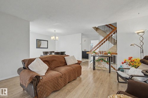 Open-concept living area featuring wood-finish flooring, a contemporary chandelier in the dining space, and a staircase with wood handrails and white balusters - 17305 60 Ave, Edmonton, AB 