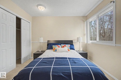 Bedroom featuring neutral wall paint, a large window with a wooded backdrop, and a closet with bifold doors - 17305 60 Ave, Edmonton, AB 