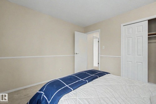Carpeted bedroom featuring neutral wall color, white trim, and a bi-fold closet with interior shelving - 17305 60 Ave, Edmonton, AB 