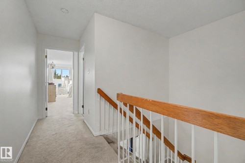 Carpeted hallway with a wood-finish handrail and white balusters - 17305 60 Ave, Edmonton, AB 