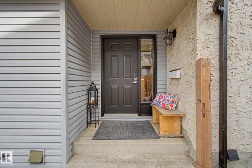 Front entry featuring a dark-paneled door with sidelight, overhead soffit, concrete steps, and a wall-mounted light fixture - 17305 60 Ave, Edmonton, AB 