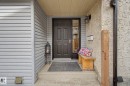 Front entry featuring a dark-paneled door with sidelight, overhead soffit, concrete steps, and a wall-mounted light fixture - 17305 60 Ave, Edmonton, AB 