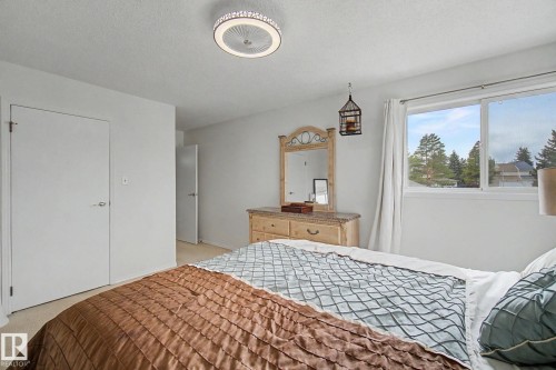 Bright bedroom featuring a large window, neutral carpeting, white walls, and a contemporary ceiling fan with integrated lighting - 17305 60 Ave, Edmonton, AB 