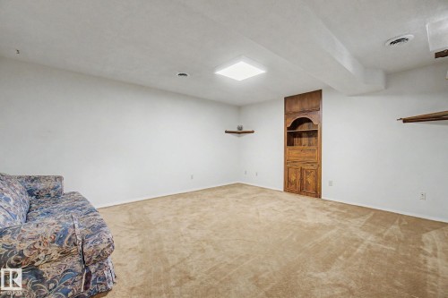 Spacious room featuring neutral carpeting, white walls, and a built-in wood cabinet with shelving - 17305 60 Ave, Edmonton, AB 