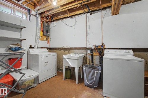 Dedicated laundry area featuring a utility sink with a dual-handle faucet, exposed ceiling joists, and a window for natural light - 17305 60 Ave, Edmonton, AB 