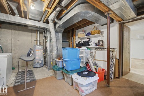 Basement utility area featuring exposed wood joists and ductwork, a concrete foundation wall, and a hot water heater - 17305 60 Ave, Edmonton, AB 