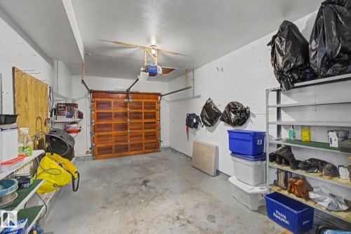 Garage space featuring a wood-panel garage door, concrete flooring, overhead lighting, and built-in shelving - 17305 60 Ave, Edmonton, AB 