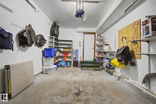 Garage interior featuring a concrete floor, white painted walls, exposed ceiling joists, a white entry door, and built-in shelving units - 17305 60 Ave, Edmonton, AB 