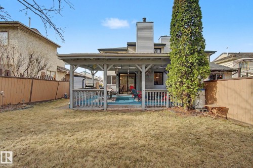 Backyard featuring a covered deck with railing, a sliding glass door, mature evergreen tree, and wood fencing - 17305 60 Ave, Edmonton, AB 