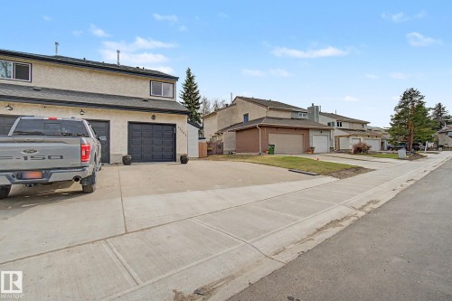 Stucco exterior with multiple windows, two black garage doors, and a concrete driveway - 17305 60 Ave, Edmonton, AB 
