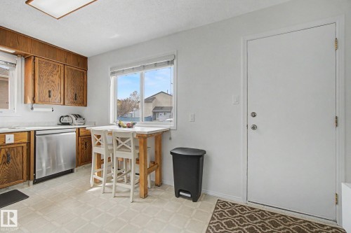 Kitchen featuring wood cabinetry, white countertops, stainless steel dishwasher, and patterned flooring - 17305 60 Ave, Edmonton, AB 