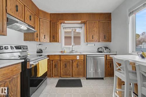 Kitchen featuring wood cabinetry, light countertops, stainless steel appliances, and a window - 17305 60 Ave, Edmonton, AB 