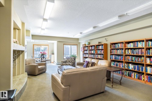 Inviting common area featuring comfortable seating, extensive built-in bookshelves, and large windows providing ample natural light - 104 612 111 Street Sw, Edmonton, AB - Indoor
