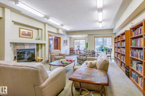 The property features a spacious room with a fireplace, extensive built-in bookshelves, and large windows that provide natural light - 104 612 111 Street Sw, Edmonton, AB - Indoor Photo Showing Living Room With Fireplace