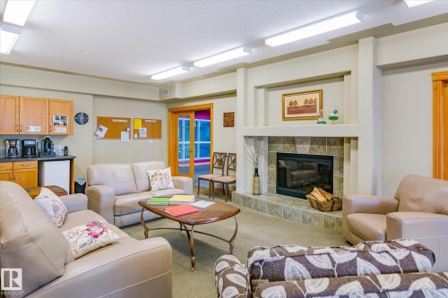 The property features a spacious room with a stone-tiled fireplace, a kitchenette with wood cabinetry, and a sliding glass door - 104 612 111 Street Sw, Edmonton, AB - Indoor Photo Showing Living Room With Fireplace