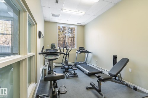 The fitness area features a selection of exercise equipment, a window with natural light, and overhead lighting - 104 612 111 Street Sw, Edmonton, AB - Indoor Photo Showing Gym Room