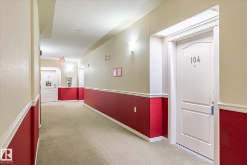 Well-lit hallway with neutral tone carpet and walls featuring a bold red lower section with white trim - 104 612 111 Street Sw, Edmonton, AB - Indoor Photo Showing Other Room