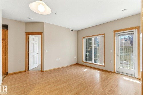 Living area featuring hardwood flooring, a ceiling-mounted light fixture, and natural light from the window and glass-paneled door - 104 612 111 Street Sw, Edmonton, AB - Indoor Photo Showing Other Room