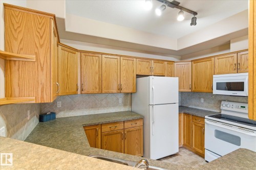 The kitchen features extensive wood cabinetry, a built-in microwave, and a white electric range - 104 612 111 Street Sw, Edmonton, AB - Indoor Photo Showing Kitchen