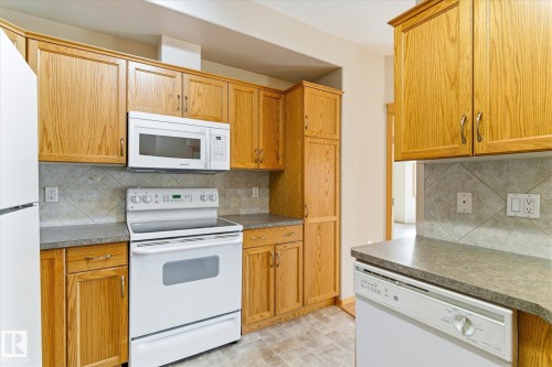 The property features a kitchen with wood cabinetry, a white electric range, a microwave, and a dishwasher - 104 612 111 Street Sw, Edmonton, AB - Indoor Photo Showing Kitchen