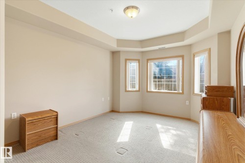 Spacious room featuring neutral-toned walls, carpeted flooring, and multiple windows with wooden trim - 104 612 111 Street Sw, Edmonton, AB - Indoor Photo Showing Other Room