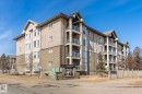 The property features a multi-story building with a neutral-toned exterior, brick detailing, and balconies with glass railings - 104 612 111 Street Sw, Edmonton, AB  - Outdoor With Facade 
