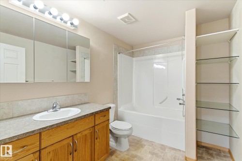 The bathroom features a vanity with a countertop and wood cabinetry, a white oval sink, and a mirrored medicine cabinet with integrated lighting - 104 612 111 Street Sw, Edmonton, AB - Indoor Photo Showing Bathroom