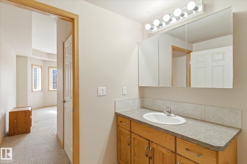 Bathroom vanity featuring a single sink, wood cabinetry, and a mirrored medicine cabinet with overhead lighting - 104 612 111 Street Sw, Edmonton, AB - Indoor Photo Showing Bathroom