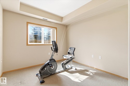This room features a window with wood trim, providing natural light, and light-colored carpeting - 104 612 111 Street Sw, Edmonton, AB - Indoor Photo Showing Gym Room