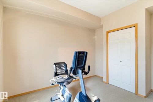 This room features neutral-toned walls, carpeted flooring, and a white bi-fold closet door with wood trim - 104 612 111 Street Sw, Edmonton, AB - Indoor Photo Showing Gym Room