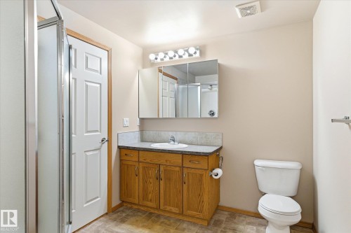 The bathroom features a shower with a clear glass enclosure, a vanity with a wood finish, a white sink, and a built-in mirror cabinet with overhead lighting - 104 612 111 Street Sw, Edmonton, AB - Indoor Photo Showing Bathroom