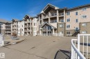 The property features a multi-story building with a stucco and stone facade, private balconies with glass railings, and an arched entryway - 104 612 111 Street Sw, Edmonton, AB  - Outdoor With Facade 