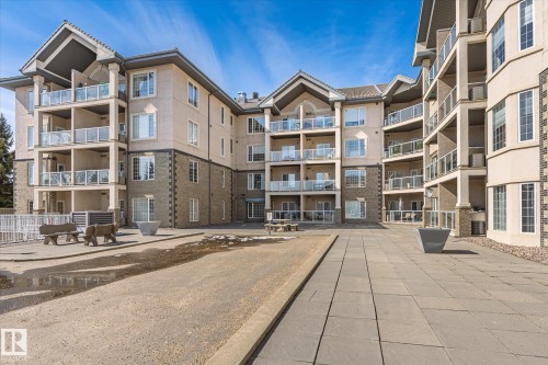 The property features a multi-story exterior with balconies, a paved patio area, and decorative stone accents - 104 612 111 Street Sw, Edmonton, AB - Outdoor With Facade
