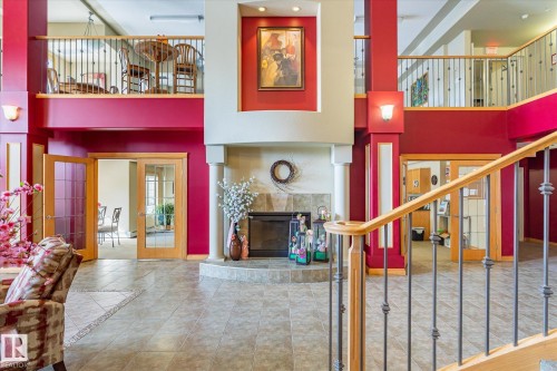 Expansive interior featuring a fireplace with decorative columns, a grand staircase with wrought iron balusters and a wooden handrail, and tiled flooring - 104 612 111 Street Sw, Edmonton, AB - Indoor Photo Showing Other Room
