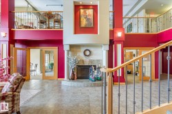 Expansive interior featuring a fireplace with decorative columns, a grand staircase with wrought iron balusters and a wooden handrail, and tiled flooring - 
