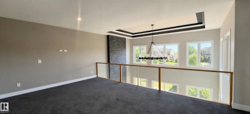 Loft area featuring dark gray carpeting, a glass railing with wood-finish top rail, and an accent wall with stacked stone finish - 53 Mockingbird Cres, Fort Saskatchewan, AB - Indoor Photo Showing Other Room