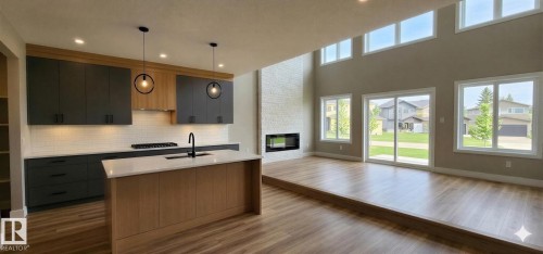 Open-concept living space featuring a modern kitchen island with a white countertop, two-tone cabinetry, wood-finish flooring, a contemporary fireplace, and abundant natural light through multiple windows - 53 Mockingbird Cres, Fort Saskatchewan, AB - Indoor Photo Showing Kitchen With Fireplace