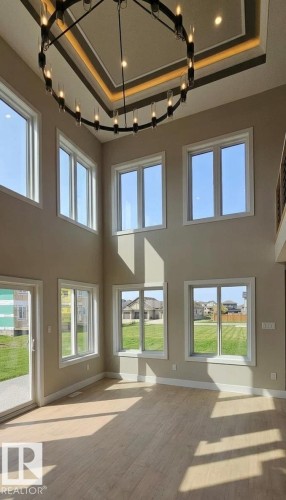 Two-story living area featuring a large circular chandelier, coffered ceiling detail, and extensive window array - 53 Mockingbird Cres, Fort Saskatchewan, AB - Indoor Photo Showing Other Room