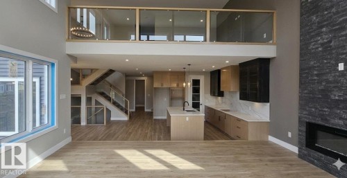 Expansive living area featuring high ceilings, wood-finish flooring, and a floor-to-ceiling dark stone fireplace with an integrated electric insert - 53 Mockingbird Cres, Fort Saskatchewan, AB - Indoor With Fireplace