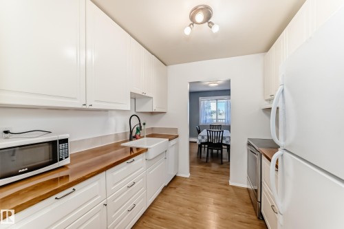 Kitchen featuring white cabinetry, wood-finish countertops, and wood-finish flooring - 423 5125 Riverbend Road, Edmonton, AB - Indoor Photo Showing Kitchen