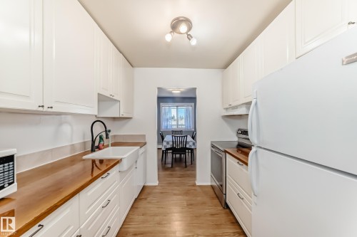 Galley kitchen featuring white cabinetry, wood-finish countertops, and wood-finish flooring - 423 5125 Riverbend Road, Edmonton, AB - Indoor Photo Showing Kitchen