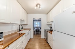 Galley kitchen featuring white cabinetry, wood-finish countertops, and wood-finish flooring - 