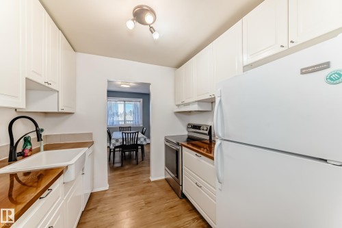 Kitchen with white cabinetry, wood-finish countertops, and wood-finish flooring - 423 5125 Riverbend Road, Edmonton, AB - Indoor Photo Showing Kitchen