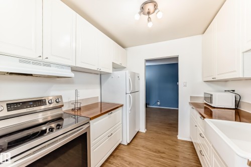 Kitchen featuring white cabinetry, wood-finish countertops, stainless steel electric range, and wood-finish flooring - 423 5125 Riverbend Road, Edmonton, AB - Indoor Photo Showing Kitchen