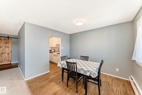 Dining space featuring wood-finish flooring, light blue wall paint, a built-in ceiling light fixture, and a window with white trim - 423 5125 Riverbend Road, Edmonton, AB - Indoor Photo Showing Dining Room