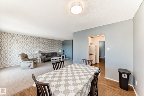 Open-concept living and dining area featuring wood-finish flooring, neutral wall paint, textured accent wall, and a pass-through to the kitchen - 423 5125 Riverbend Road, Edmonton, AB - Indoor Photo Showing Dining Room